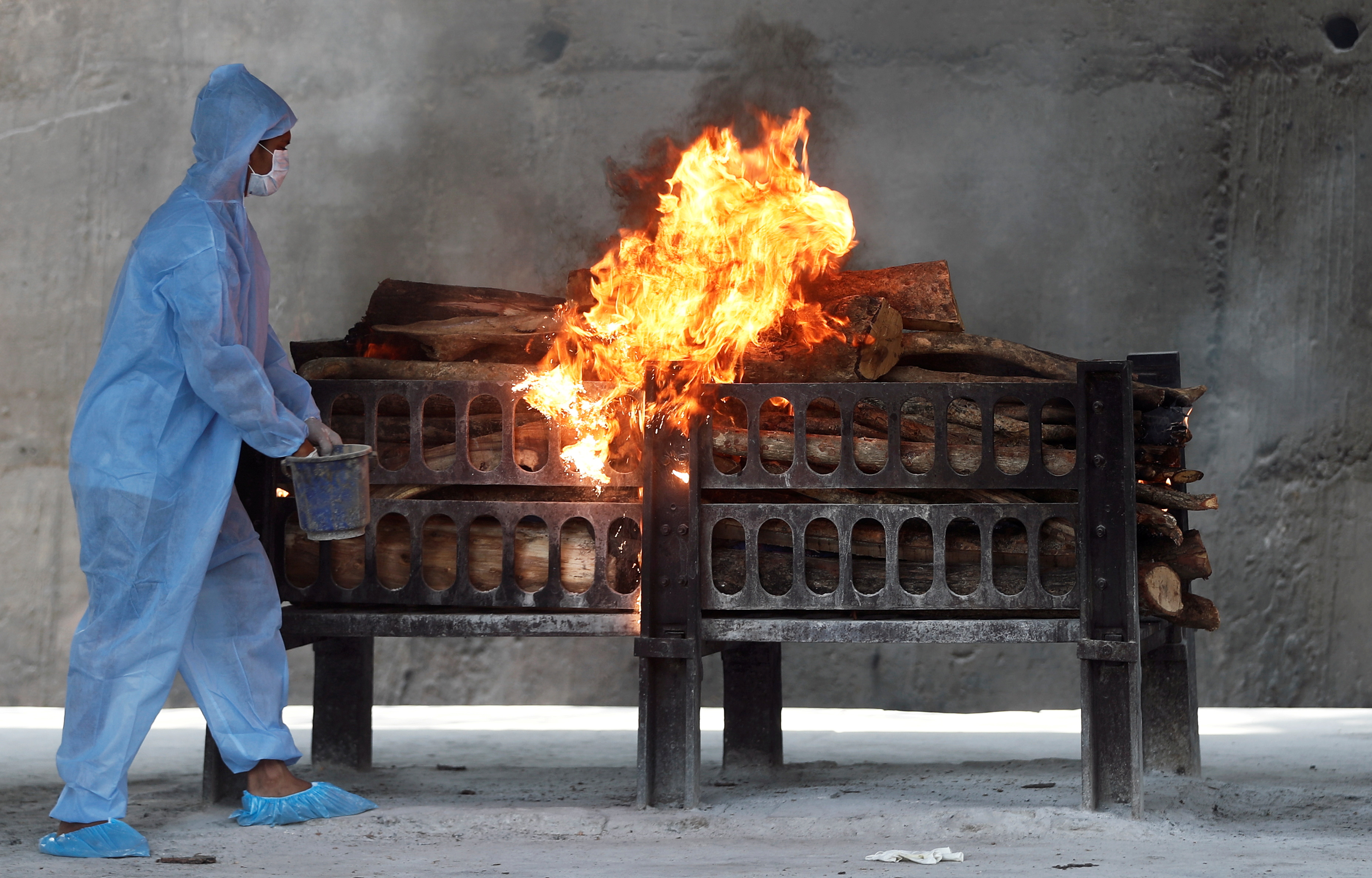 A frontline worker in personal protective equipment (PPE) sprays a flammable liquid on a burning funeral pyre of a man who died from the coronavirus disease  (COVID-19), at a crematorium on the outskirts of Mumbai India, April 15, 2021. REUTERS/Francis Mascarenhas/File Photo