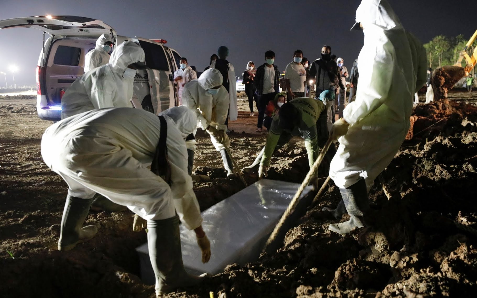 Gravediggers in PPE bury a Covid-19 victim as relatives watch from a distance at a government burial area in Jakarta