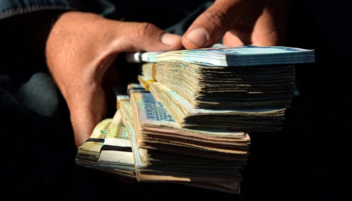 A money changer holds afghani banknotes at a currency exchange market. — AFP/File