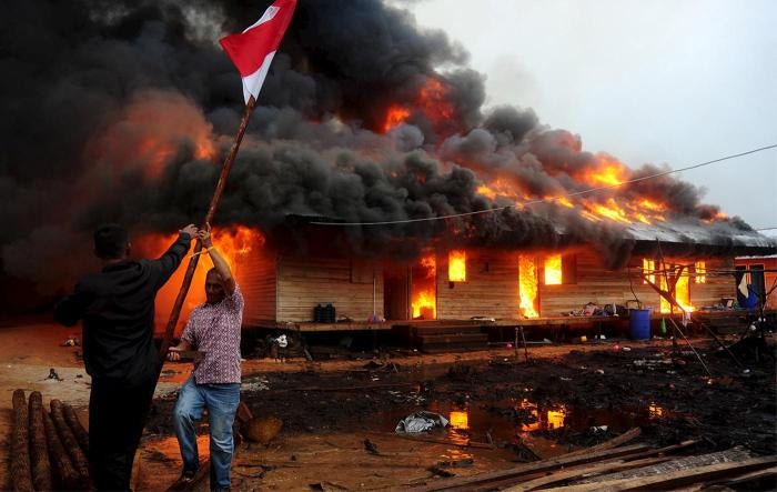 Two men hold the Indonesian flag as the compound of the Gafatar sect burns after being set on fire by local villagers, at Antibar village, West Kalimantan province, on January 19, 2016. 