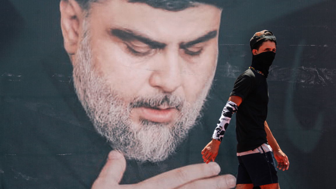 A youth walks in front of a large poster of Iraq's populist Shia cleric Moqtada Sadr, in Sadr City, east of the capital Baghdad, on 15 July 2021. [Getty] 