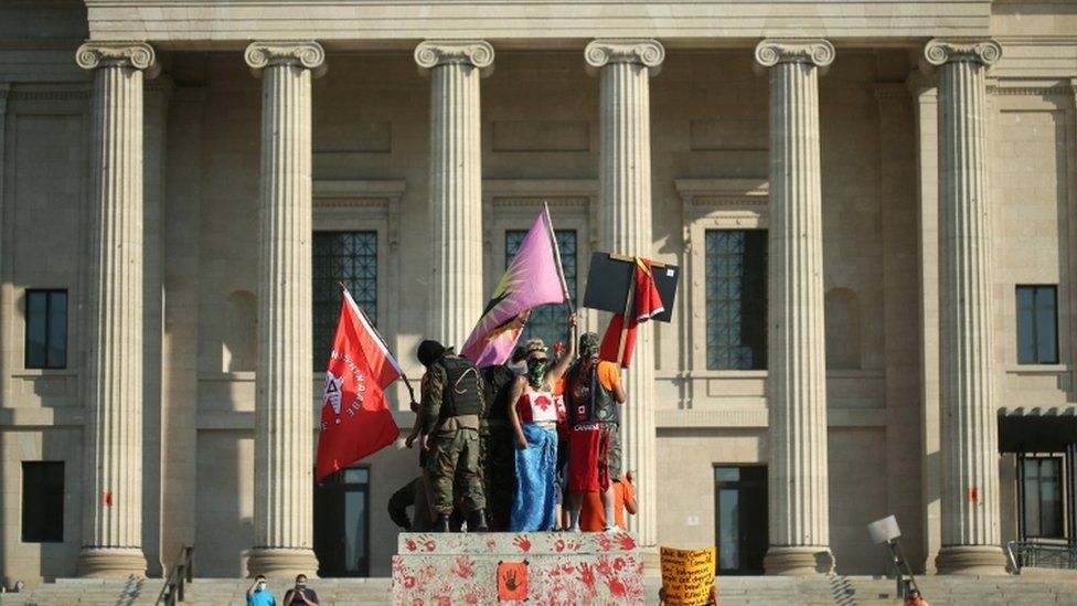 Protesters stand on a pedestal that once supported a statue of Queen Victoria