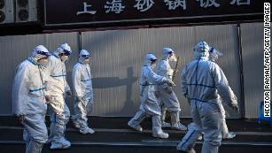 Workers in  protective clothes walk past barriers placed to close off streets in areas locked down after the detection of cases of Covid-19 in Shanghai on March 15, 2022.