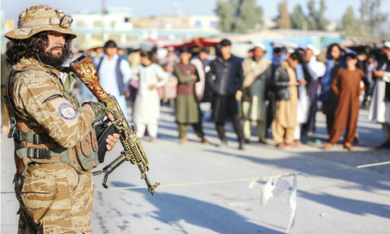 An Afghan security official stands guard at Torkham border as Afghan people wait to cross into Pakistan. — AFP