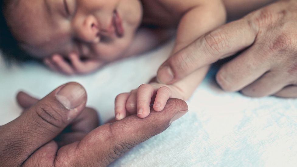 A baby with two adult hands touching (Credit: Getty Images)