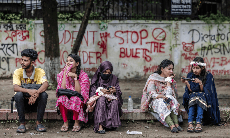 Bangladeshi students hang out together in front of a wall with graffitis against the government and the police brutality made by protesters in front of the Shaheed Minar in Dhaka on Aug 11, 2024. — AFP