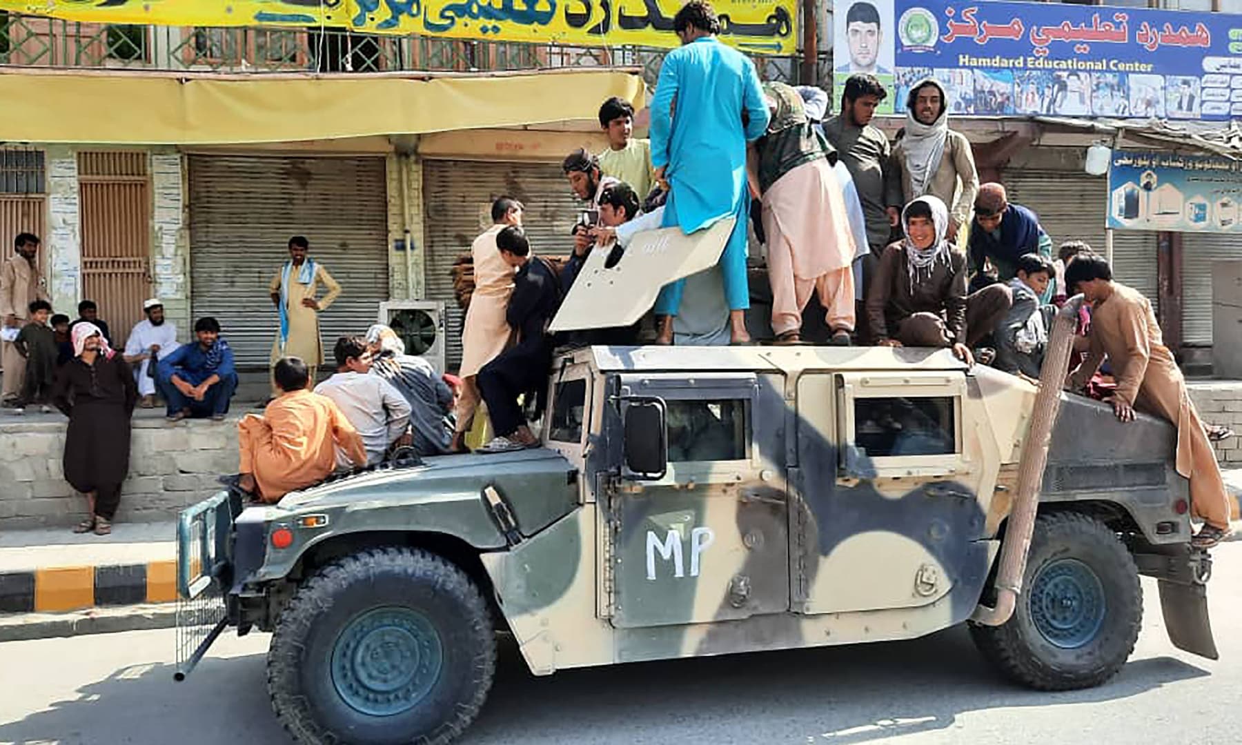 Taliban fighters and local residents sit over an Afghan National Army humvee vehicle along the roadside in Laghman province, Afghanistan on August 15, 2021. — AFP