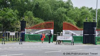 Two people walk through guarded gate painted with colors of Indian flag. In front of gate is a long barrier and signs saying stop