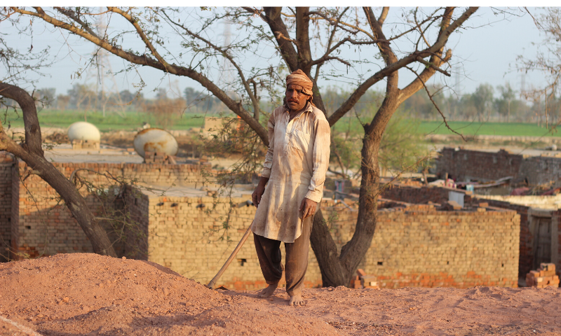 As the stacking of bricks is being done, a labourer covers it with soil.