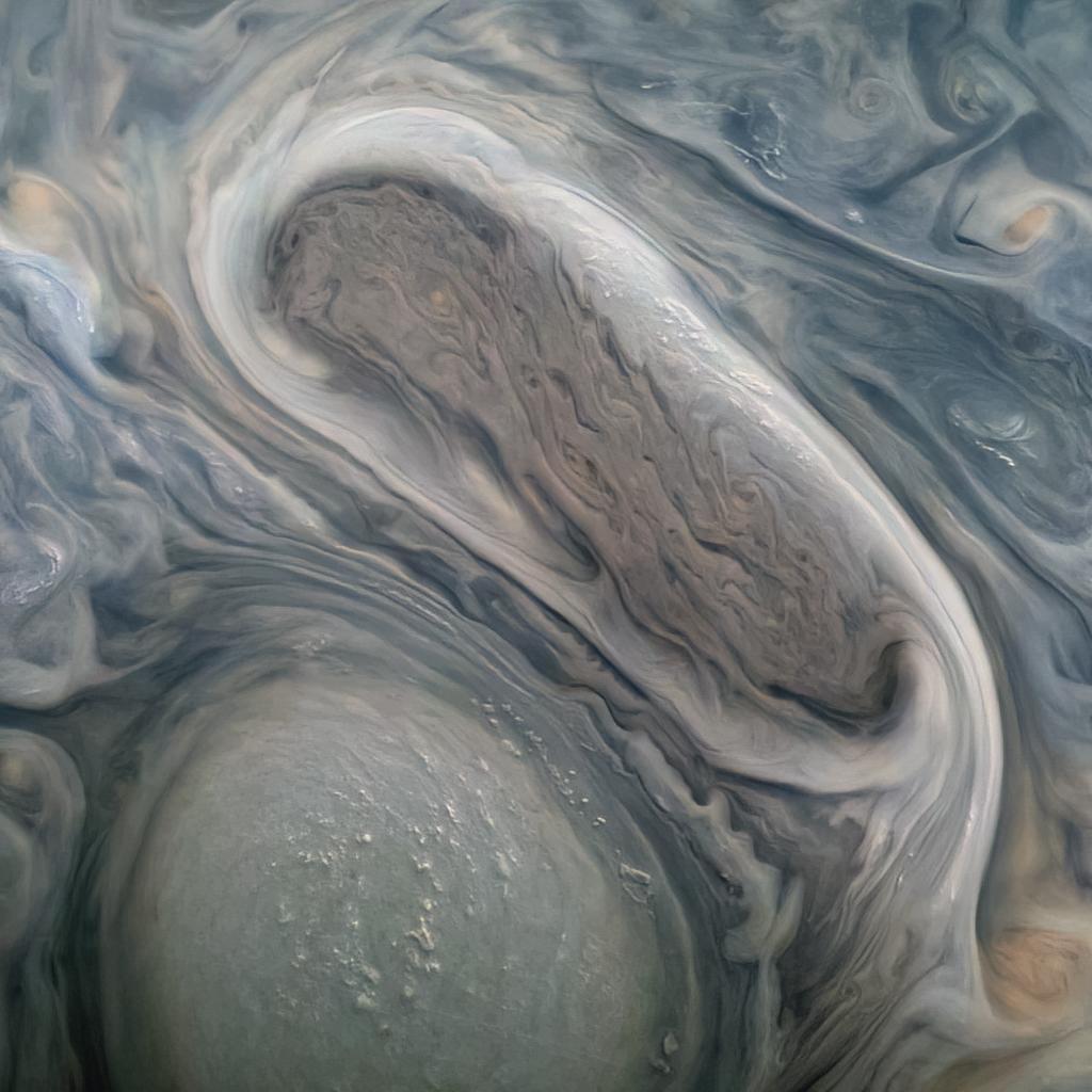 An image captured by NASA's Juno orbiter showing two of Jupiter's massive rotating storms — a swirl of gray-and-blue-tinged clouds — as viewed from orbit.