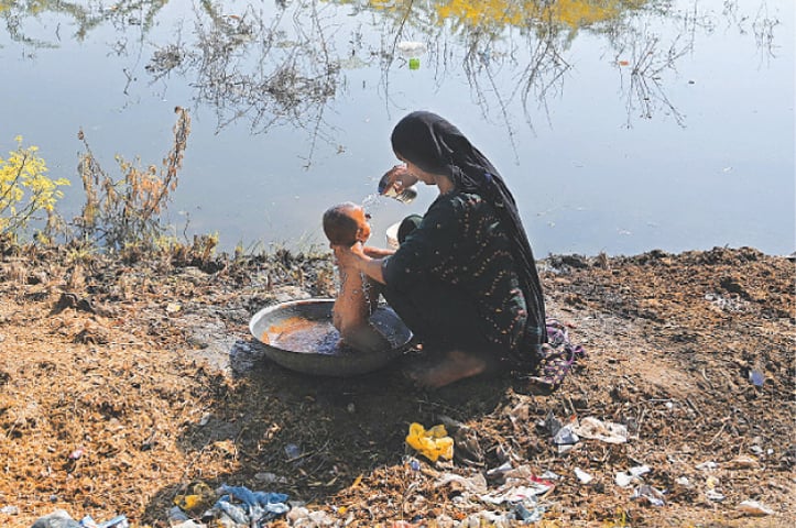 An internally displaced flood-affected woman bathes her child at a makeshift camp in Mehar city after heavy monsoon rains in Dadu district, Sindh.—AFP