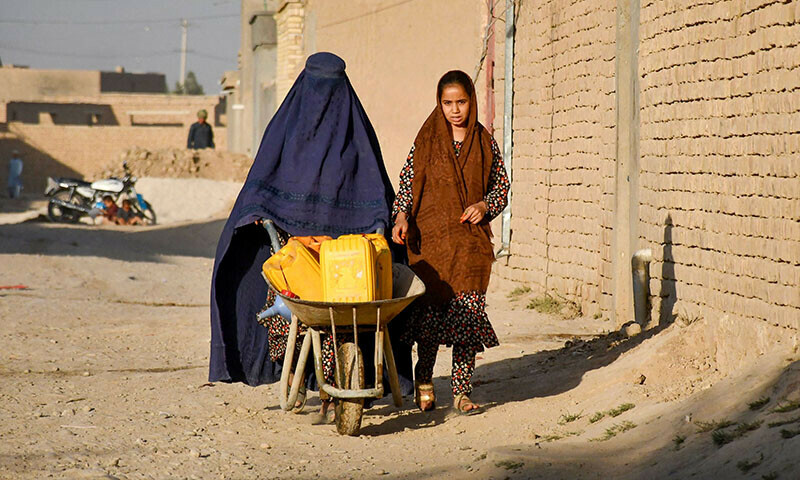 An Afghan burqa-clad woman pushes a wheelbarrow, on the outskirts of Mazar-i-Sharif on September 25. — AFP