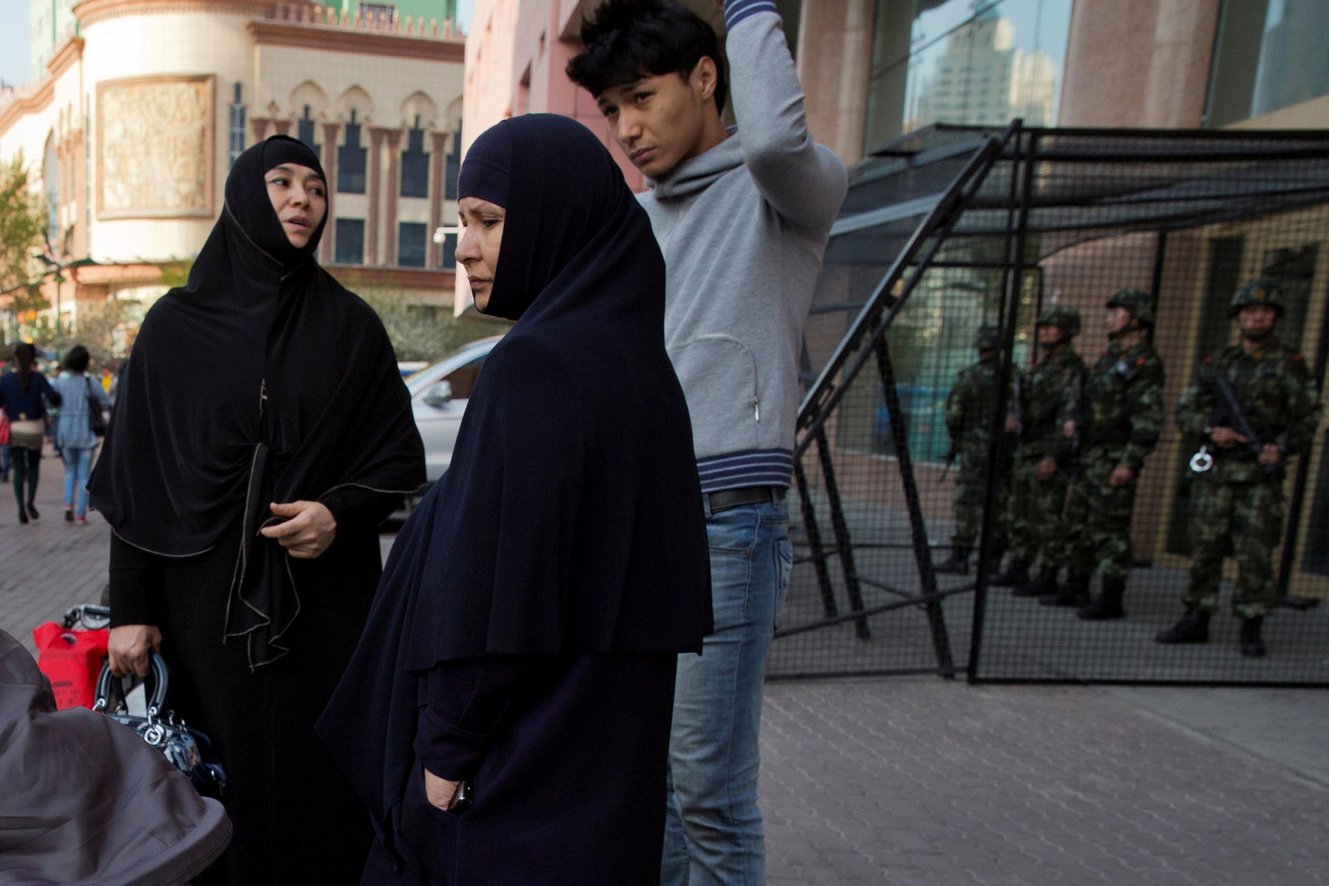 Uighur women standing near a cage protecting heavily armed Chinese paramilitary policemen on duty in China's northwestern region of Xinjiang, May 1, 2014.