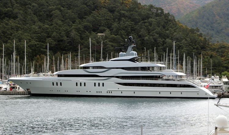 a very large yacht named Tango is docked at port with sailboat masts and trees behind it