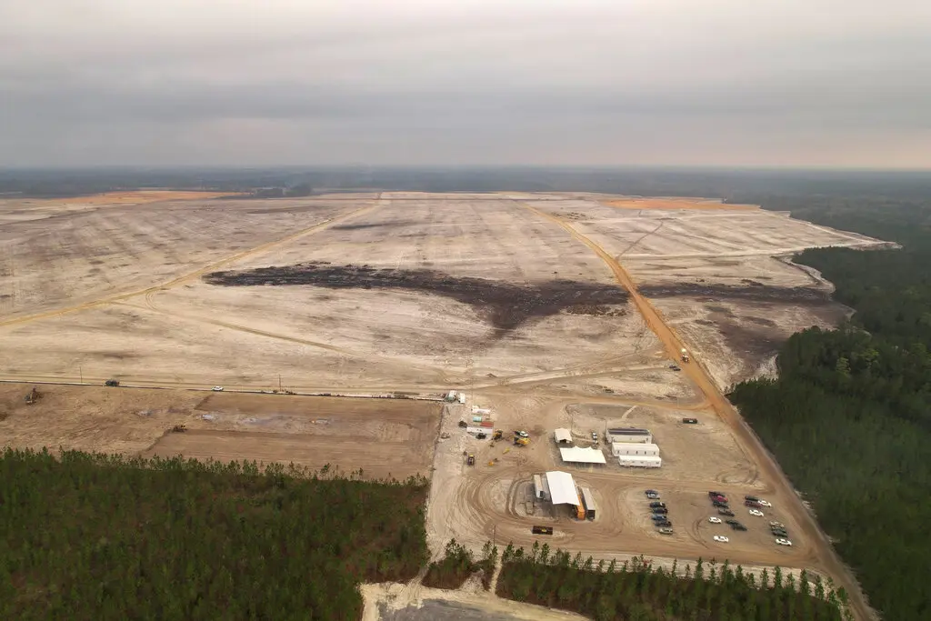 An overhead view of the mostly barren planned site of a large manufacturing plant, surrounded by trees.