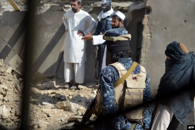 FILE - Taliban officials stand in front of remnants of a suspected Islamic State hideout following an operation against Islamic State-Khorasan, the local chapter of the jihadist group, in Kandahar, Afghanistan, Nov. 15, 2021.