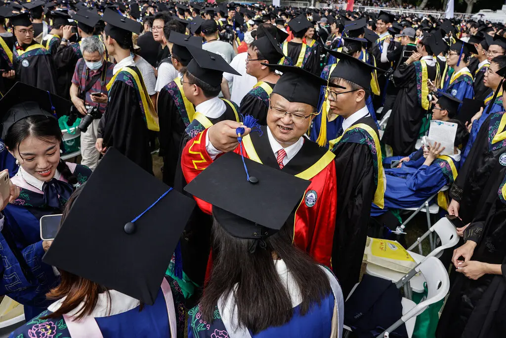 A large crowd of students wearing caps and gowns gathered at an outdoor graduation ceremony.