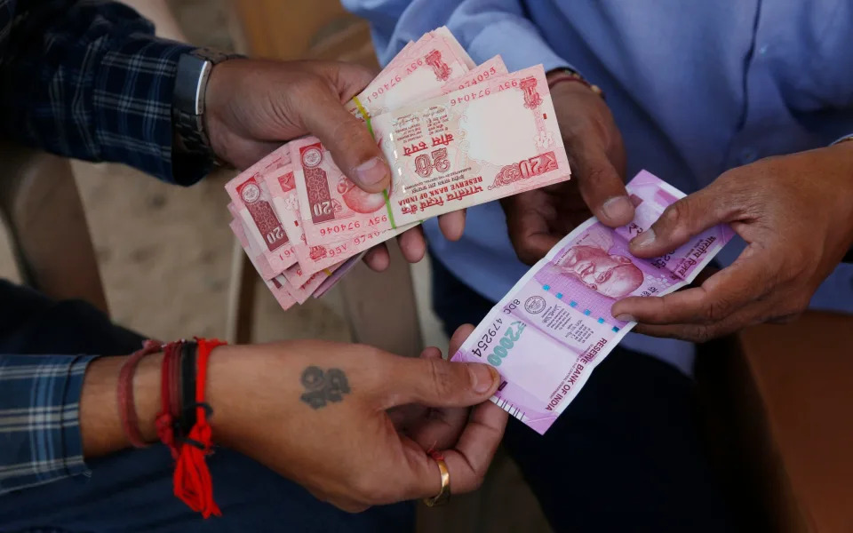 Men trade buy and sell Indian rupees at a roadside stall set up by Shri Jalaram Gaushala, a shelter for cows, in Ahmadabad, India - Ajit Solanki/AP