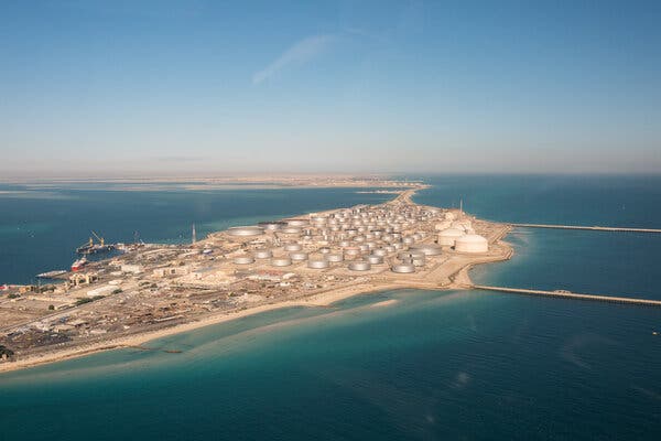 An oil tank farm, on a large swathe of sand in the middle of calm blue waters.