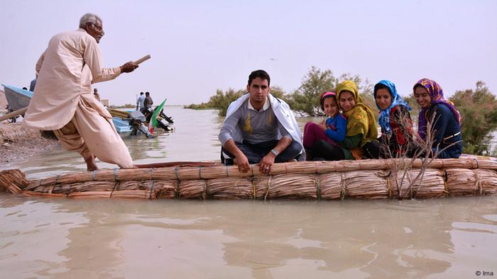 People sitting in a reed boat, a man who is standing pushes a pole to move the boat across a lake 