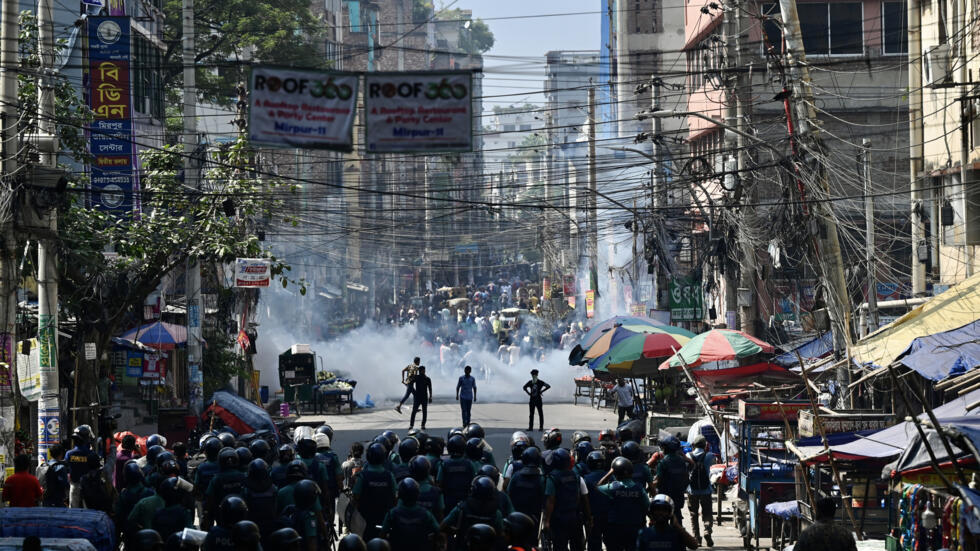 Bangladesh police (foreground) stand guard clashes with garment workers (top)demanding higher wages