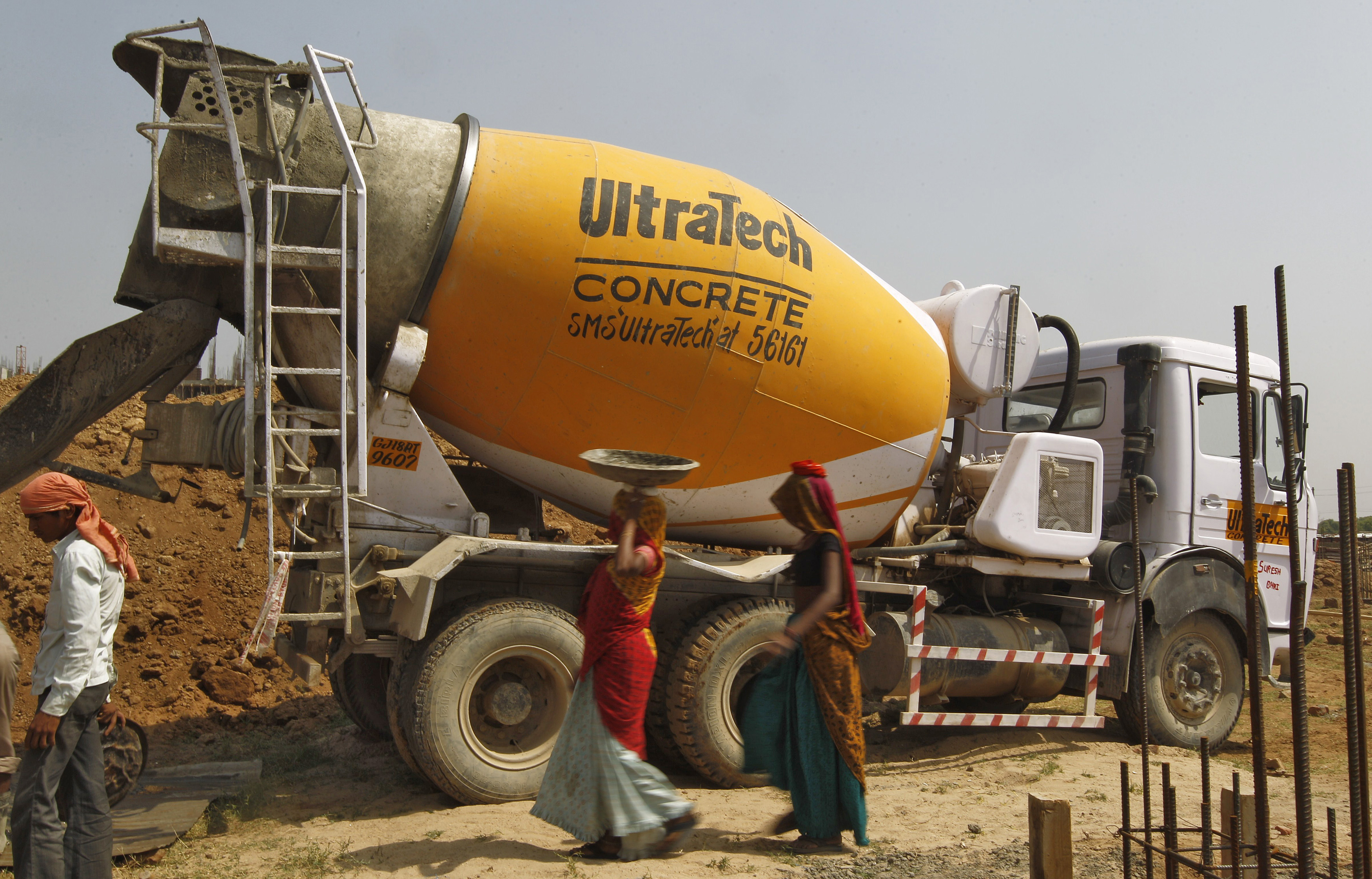 Workers walk in front of an UltraTech concrete mixture truck at the construction site of a commercial complex on the outskirts of  Ahmedabad