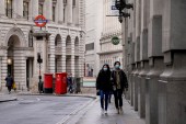 People wear face masks while walking in an empty street in London [Alberto Pezzali/AP Photo]