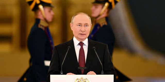 Vladimir Putin delivers an address while flanked by men in military uniforms.