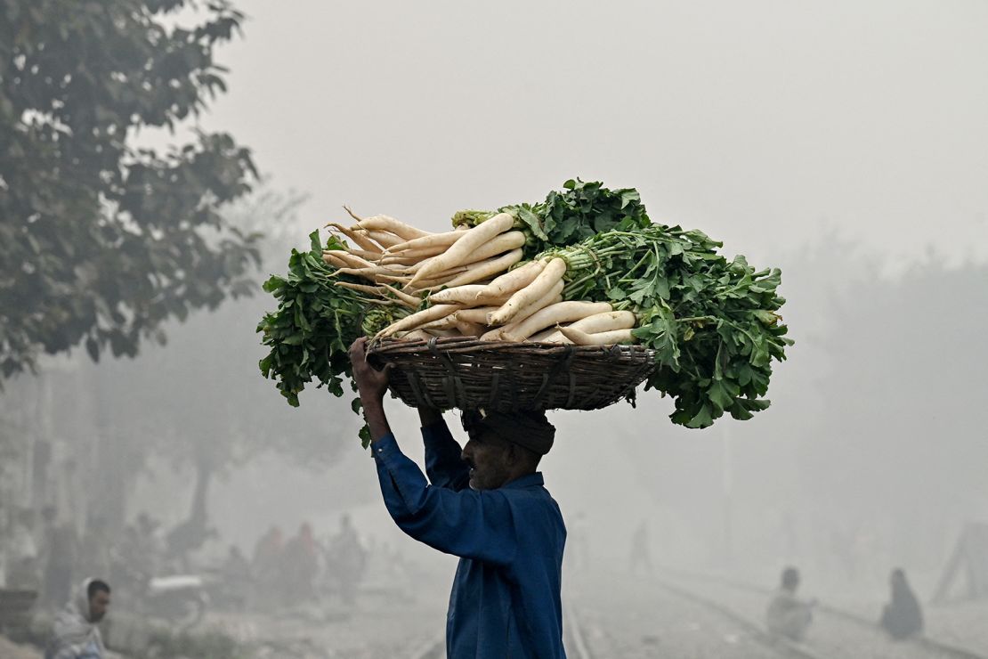 A vendor carries a basket of radishes across a railway track engulfed in smog in Lahore on November 8, 2024.